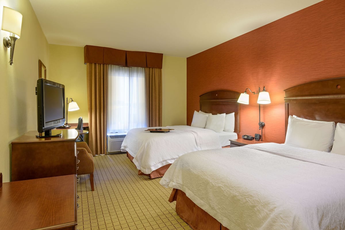 A hotel room with two beds, a desk with a television, a lamp, and a window with curtains.