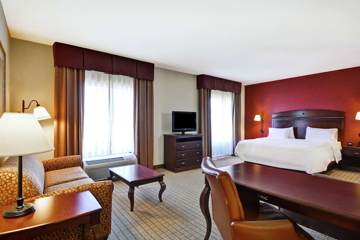 A hotel room with a bed, a desk, a chair, a television, and a desk lamp.