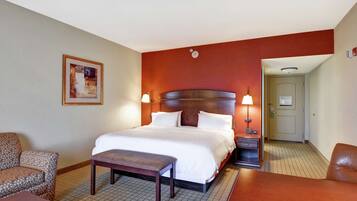A hotel room with a large bed, a chair, a desk, and a small table.