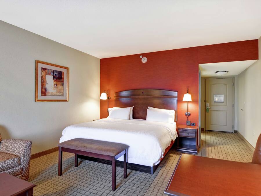 A hotel room with a large bed, a chair, a desk, and a small table.