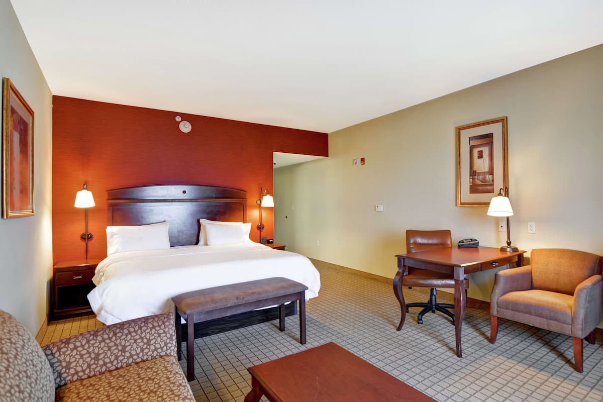 A hotel room with a large bed, a desk, two chairs, and a small table.