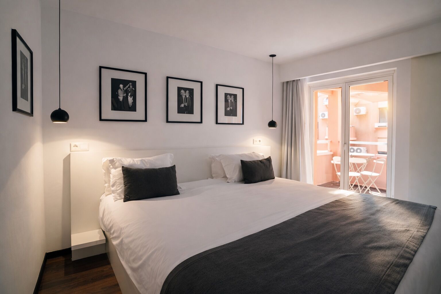 A bedroom with a bed, a bedside table, a window with curtains, and framed pictures on the wall.
