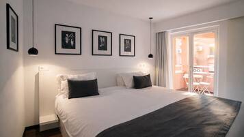A bedroom with a bed, a bedside table, a window with curtains, and framed pictures on the wall.