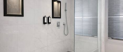 A modern bathroom with a glass-enclosed shower, marble flooring, and a large window with blinds.