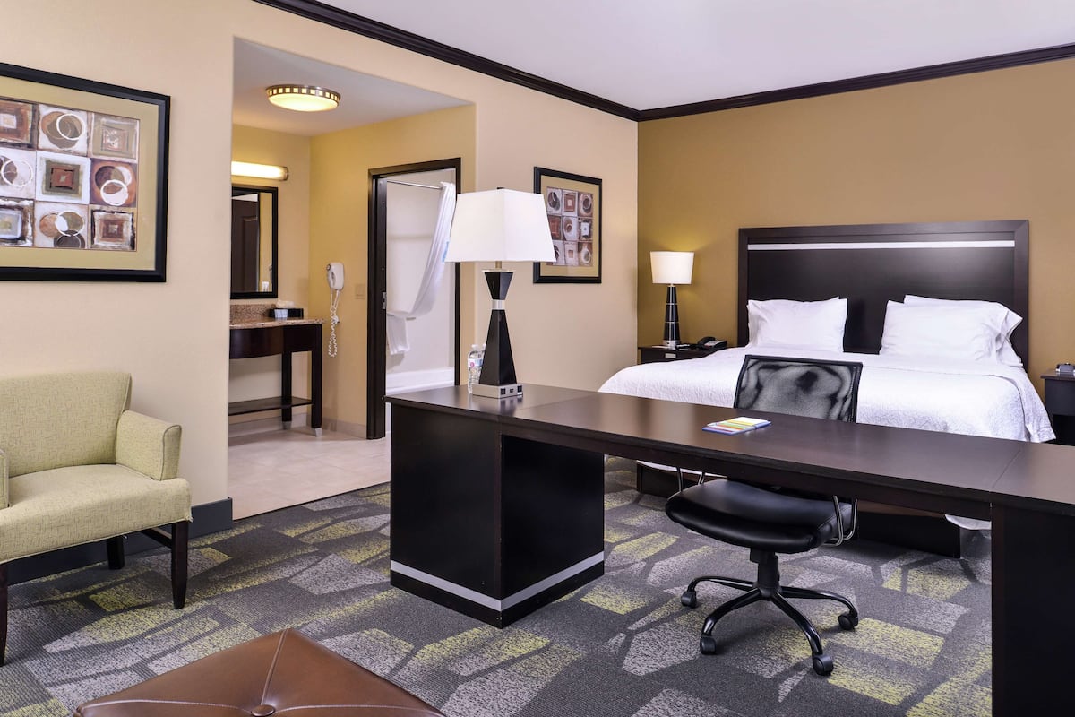 Habitación de hotel con cama, escritorio, silla y baño con ducha.
