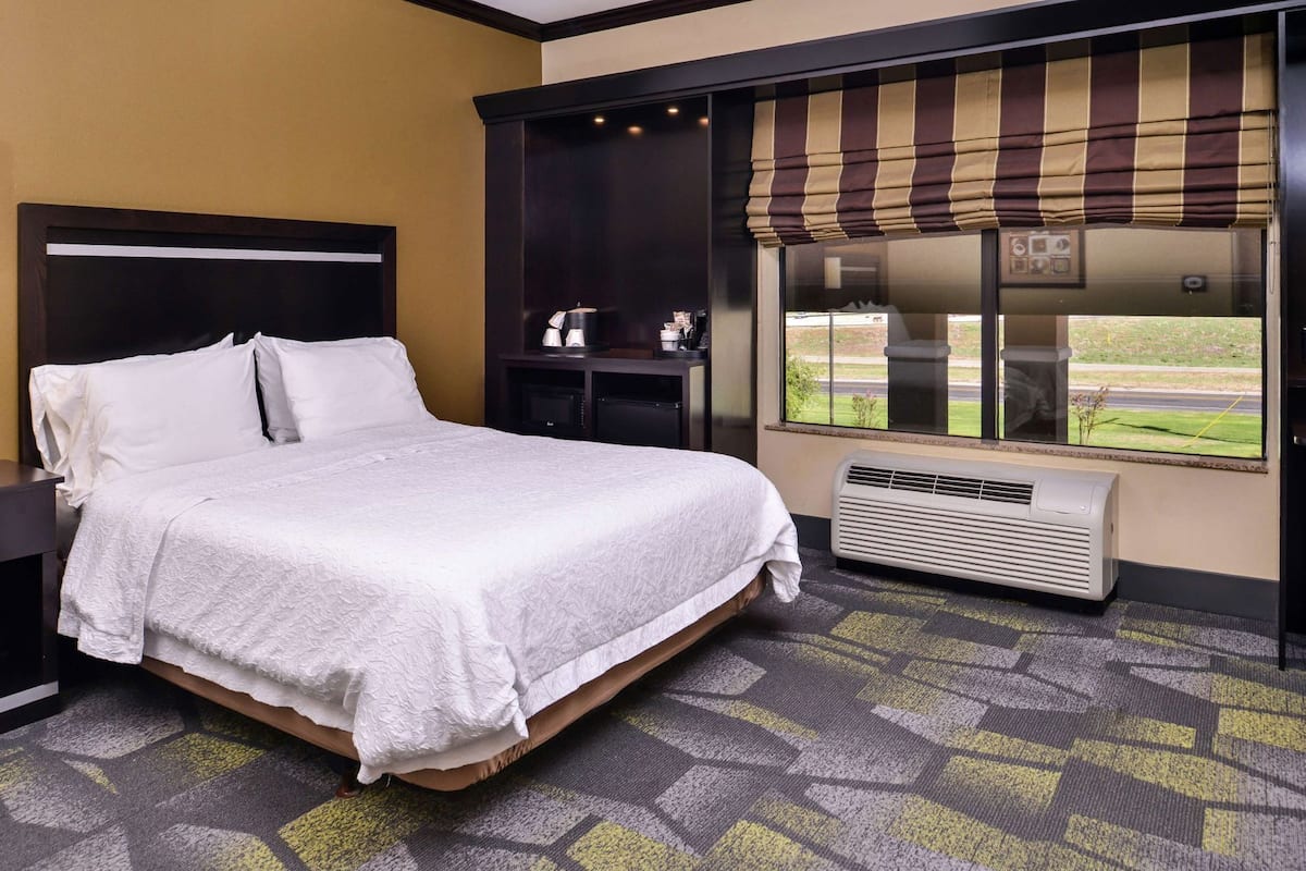 Una habitación de hotel con cama, mesita de noche, ventana con vistas y termostato.