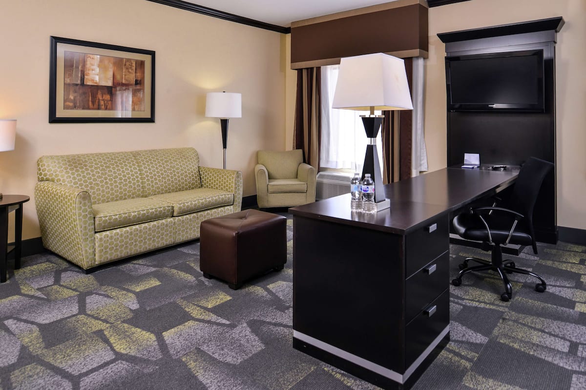 Una habitación de hotel con sofá, sillón, escritorio, lámpara y televisión.