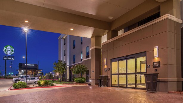 A hotel entrance with a Starbucks drive-thru, a parking lot, and a building with a glass facade. - Hampton Inn & Suites Big Spring (Big Spring)