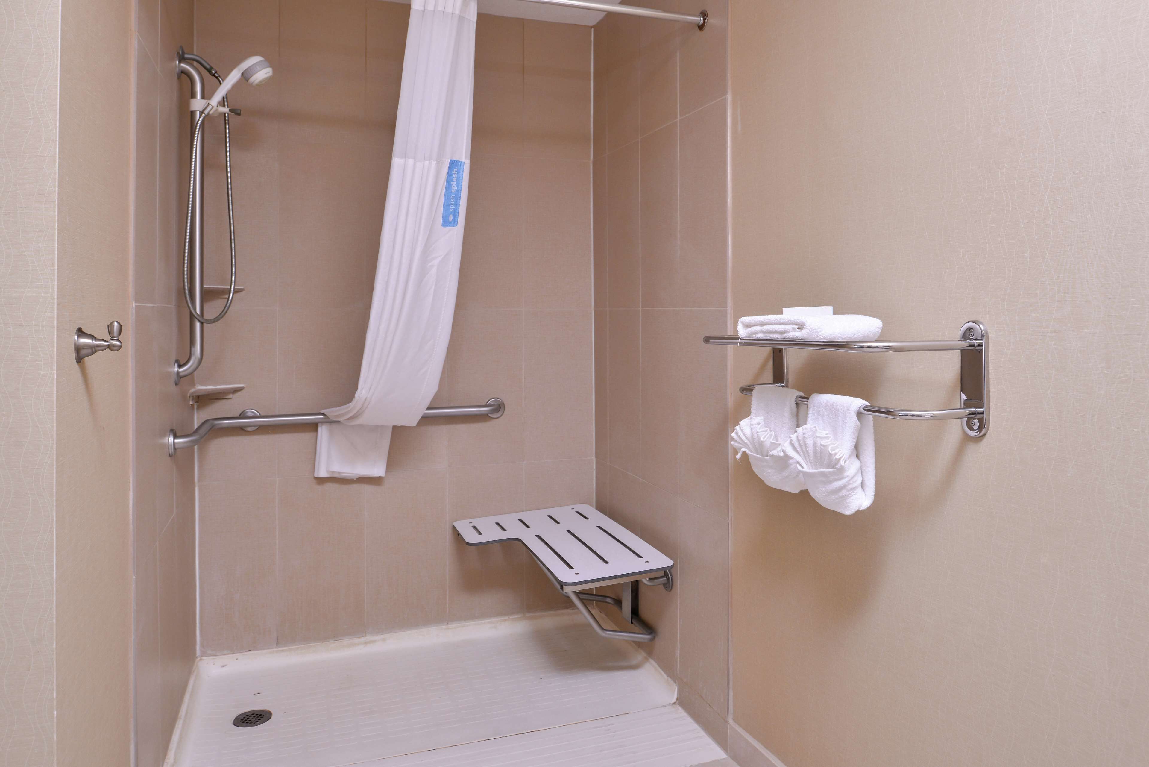 A shower area with a grab bar, a white shower curtain, and a towel rack with towels.