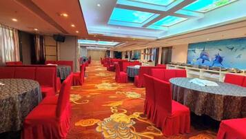A banquet hall with round tables and red chairs, a patterned carpet, and a ceiling with skylights.