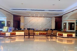 A hotel reception area with a marble wall, wooden reception desk, and several chairs. - Dihao Hotel (Quanzhou)