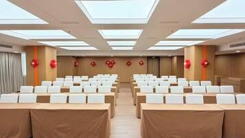 A conference room with rows of tables and chairs, large windows, and red decorative elements.