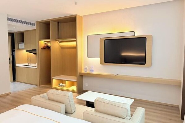 A modern hotel room with a sofa, a TV mounted on the wall, and a walk-in closet.