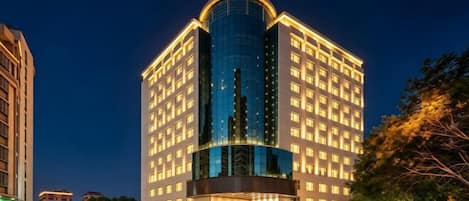 A multi-story hotel with a prominent curved glass facade, illuminated signage, and a well-lit entrance.