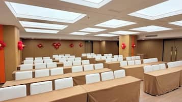 A conference room with rows of white chairs, tables covered with brown tablecloths, and a high ceiling with skylights.
