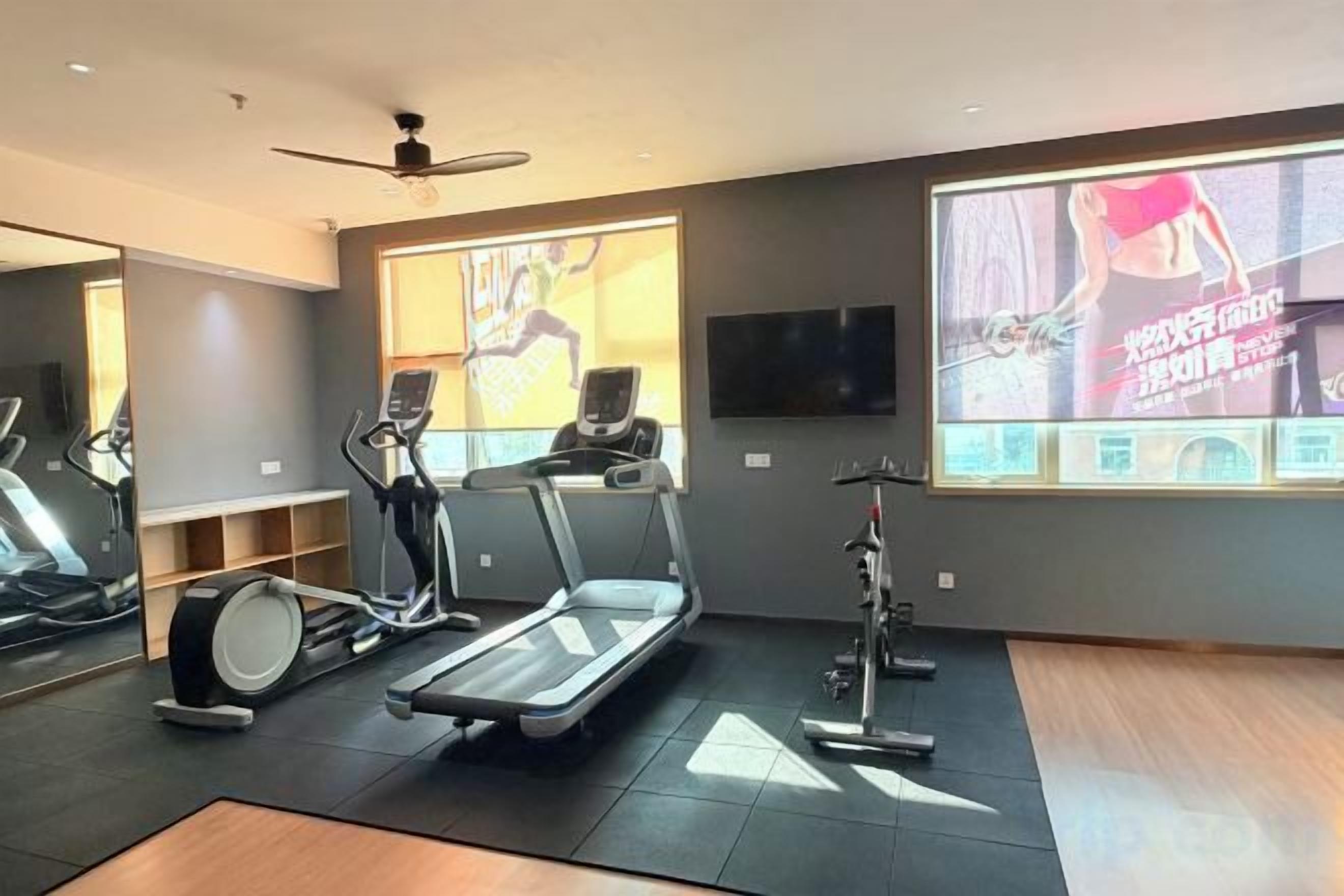 Un gimnasio con cintas de correr, bicicletas estáticas y una pantalla grande que muestra contenido de entrenamiento.