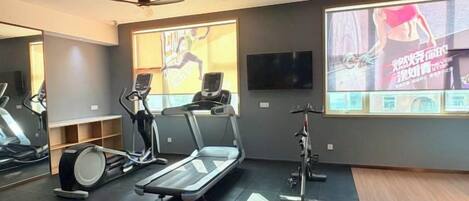 Un gimnasio con cintas de correr, bicicletas estáticas y una pantalla grande que muestra contenido de entrenamiento.