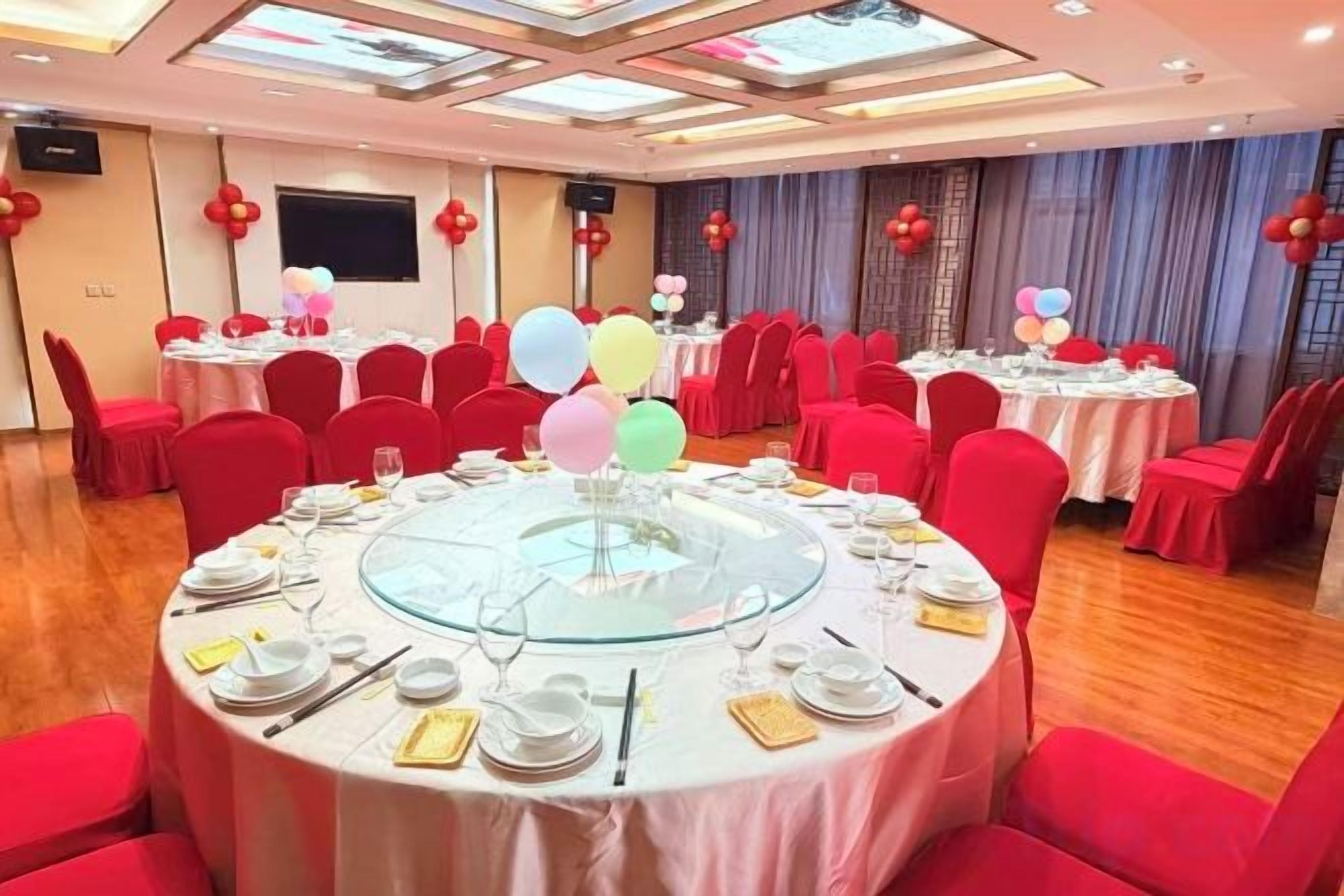 A banquet hall with round tables, red chairs, and balloons.