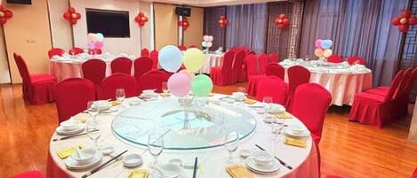 A banquet hall with round tables, red chairs, and balloons.