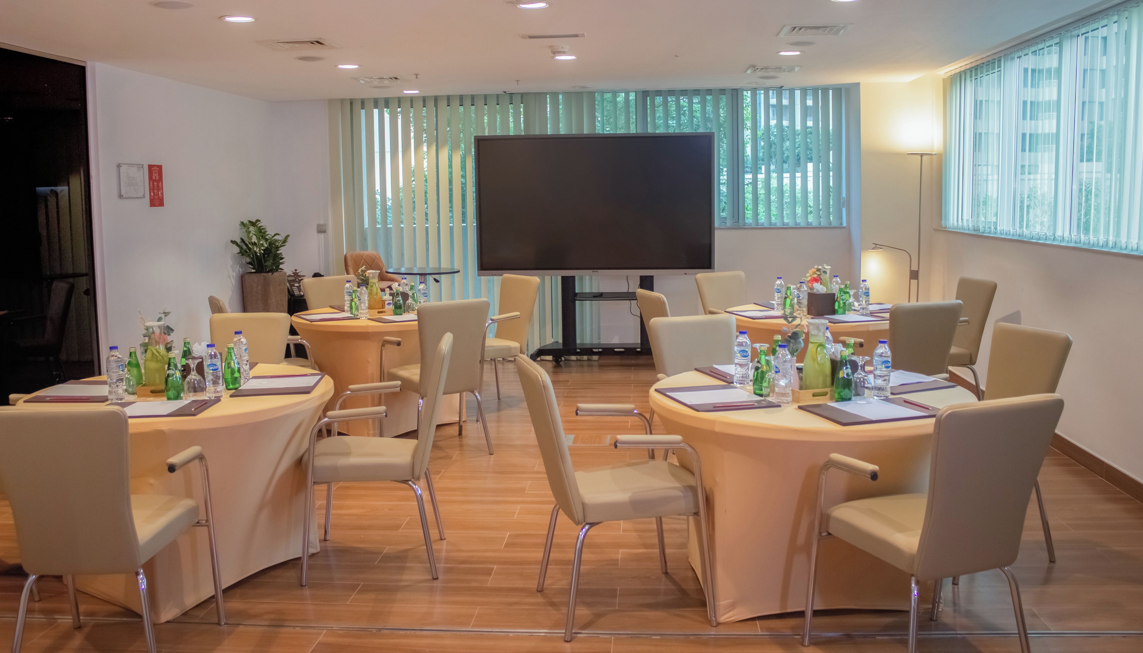 A conference room with round tables, chairs, a large screen, and a potted plant.