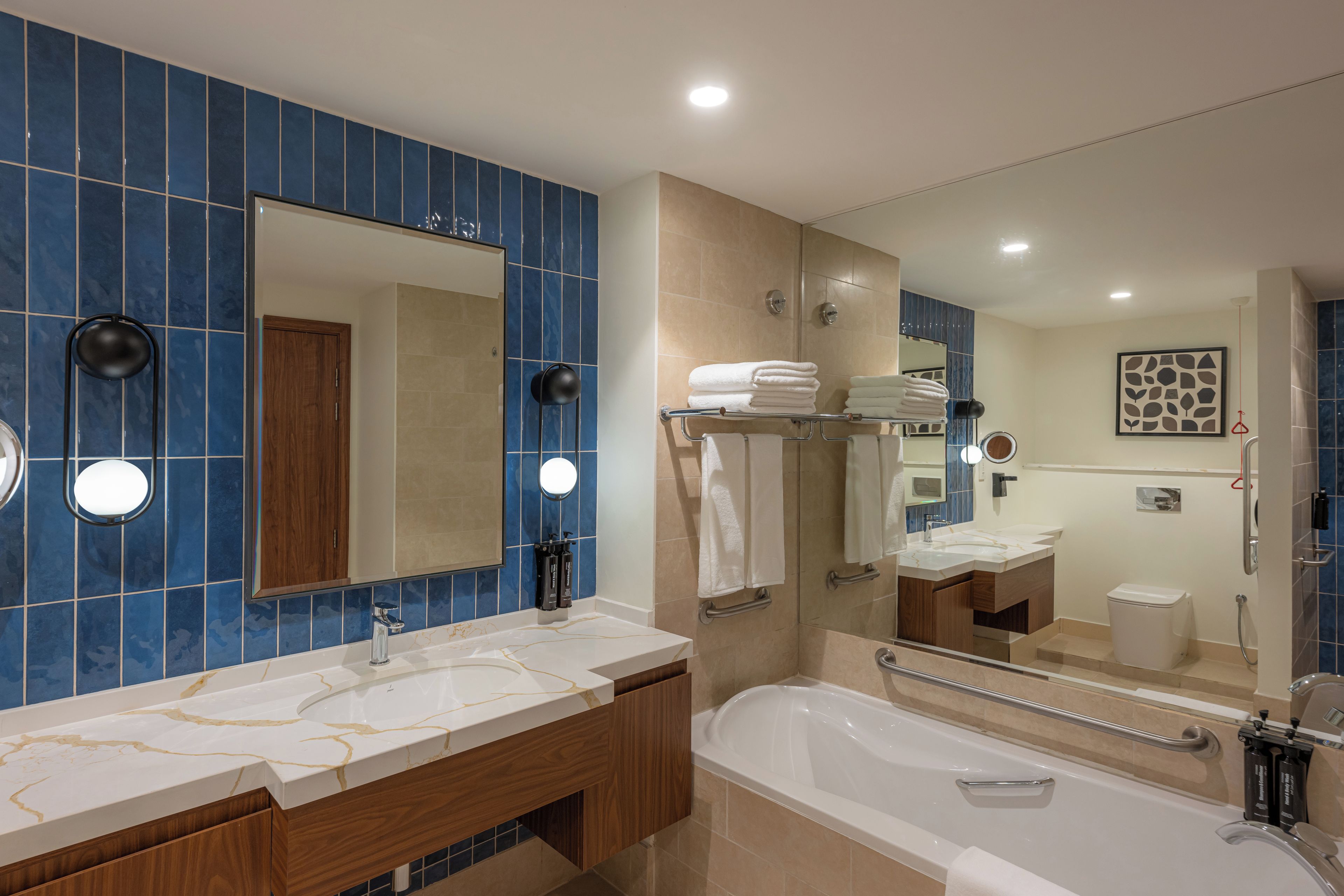 A modern bathroom with a large mirror, two sinks, a bathtub, and a shower.