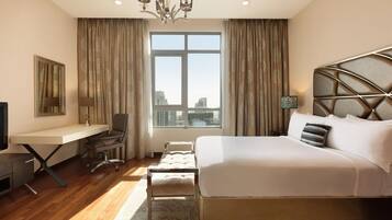 A hotel room with a bed, desk, chair, and a large window with a view of buildings.