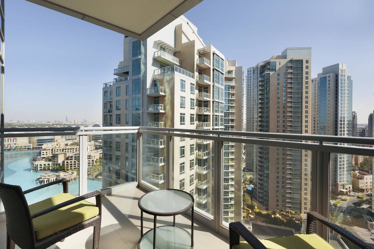Een balkon met een glazen tafel en stoelen, met uitzicht op een zwembad en hoge gebouwen.
