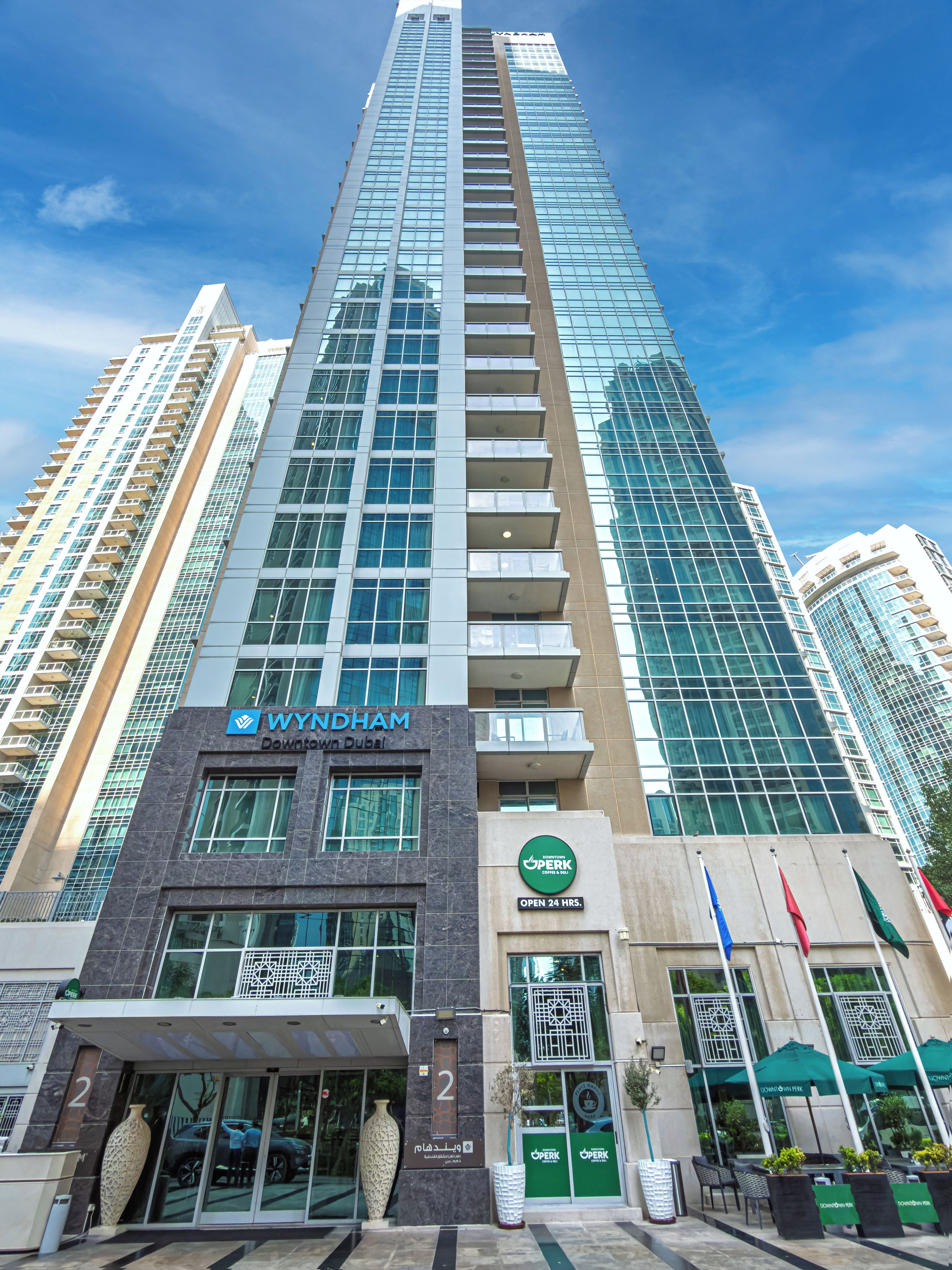 A high-rise building with a prominent Wyndham Downtown Dubai sign, a green Operk logo, and a 24-hour service notice.