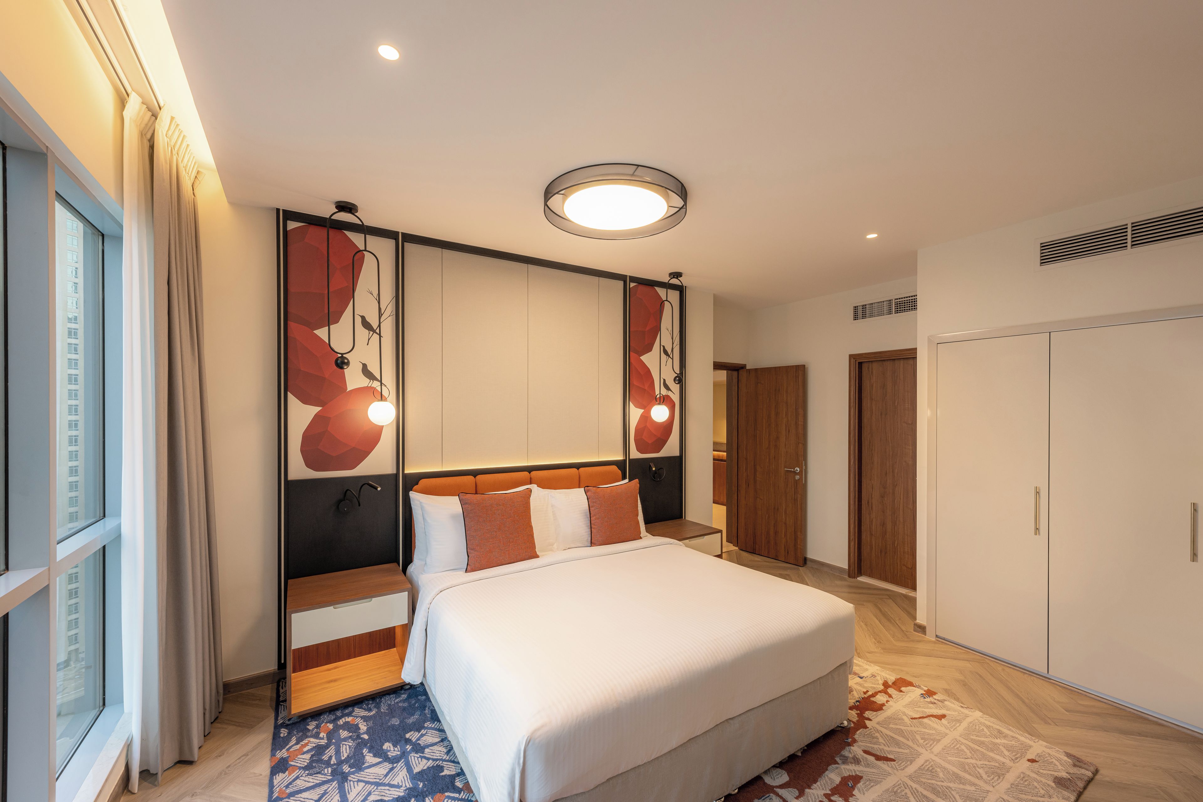 A modern hotel room with a large bed, a view of the city, and a large wardrobe.