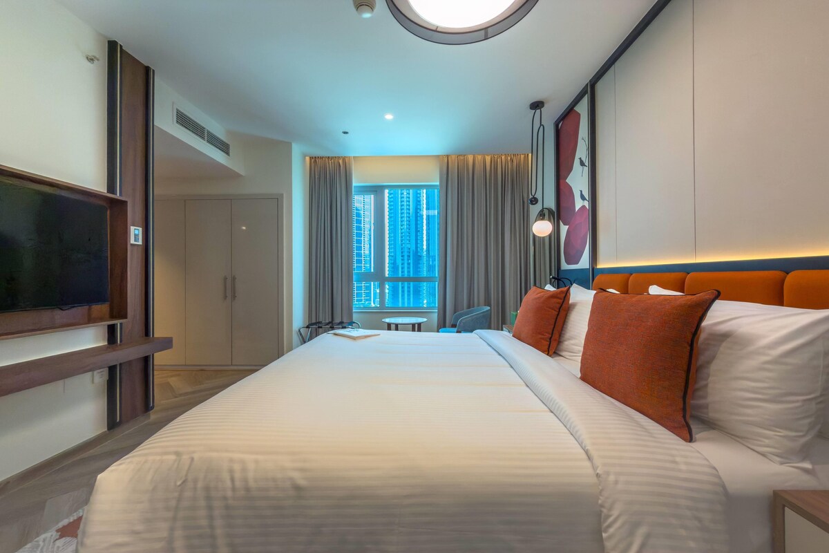 Een hotelkamer met een groot bed, een televisie, een bureau en uitzicht op de stad.