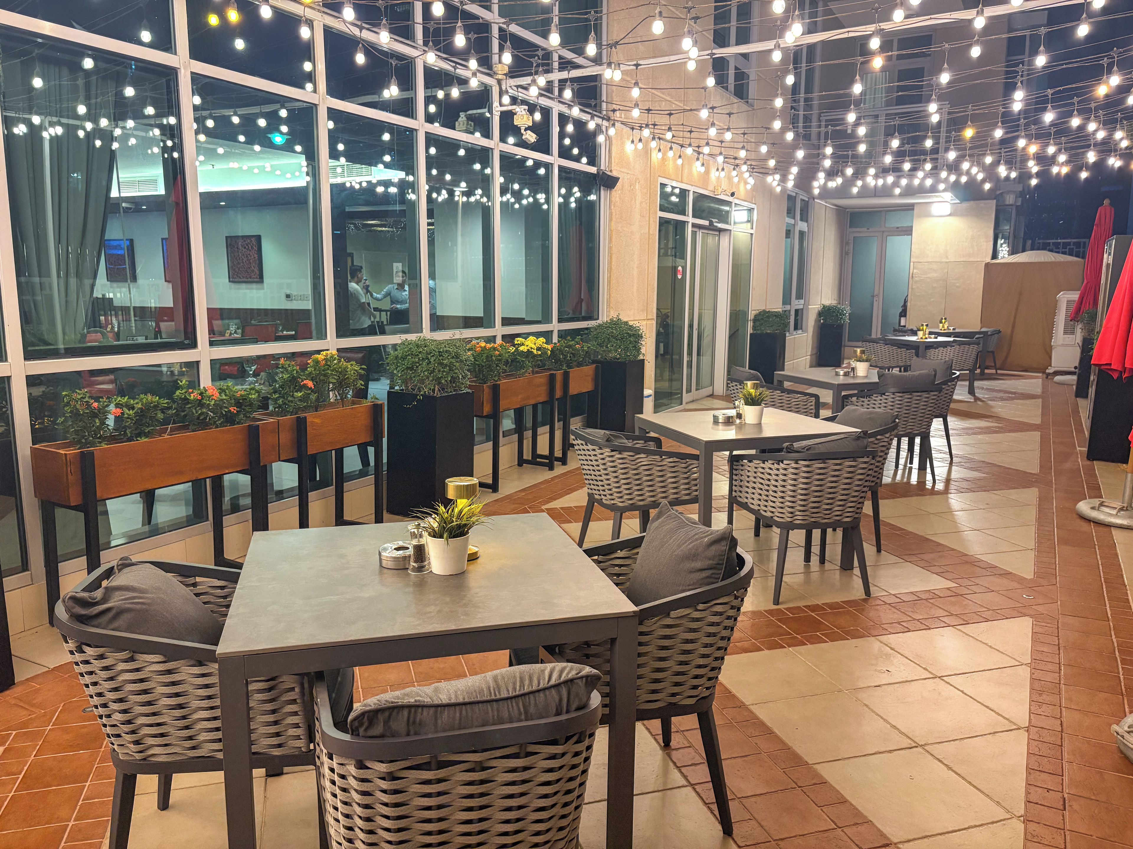 Un comedor interior con mesas y sillas, plantas en macetas y un moderno candelabro.