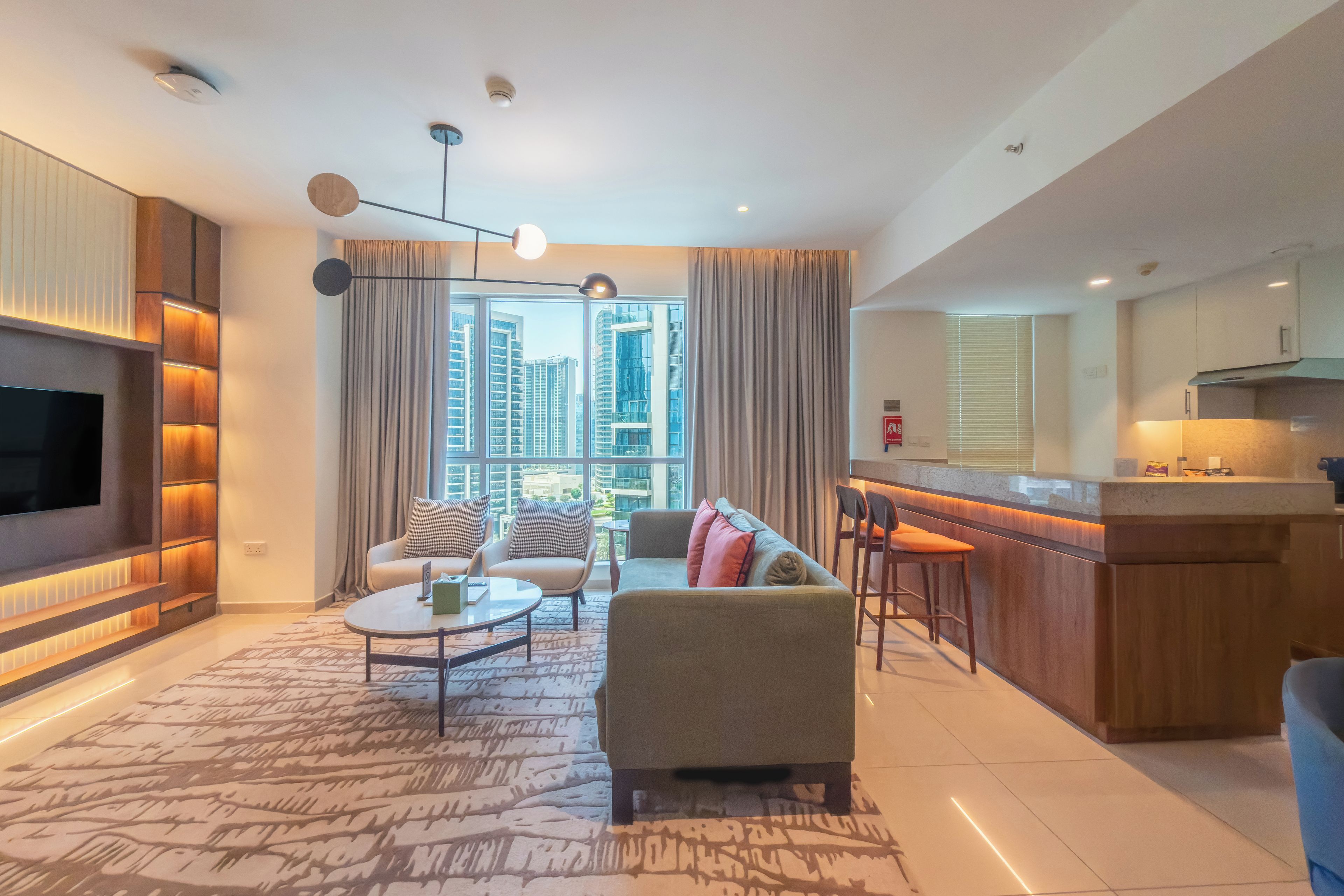 A modern living room with a flat-screen TV, a sofa, a coffee table, and a dining area with bar stools.