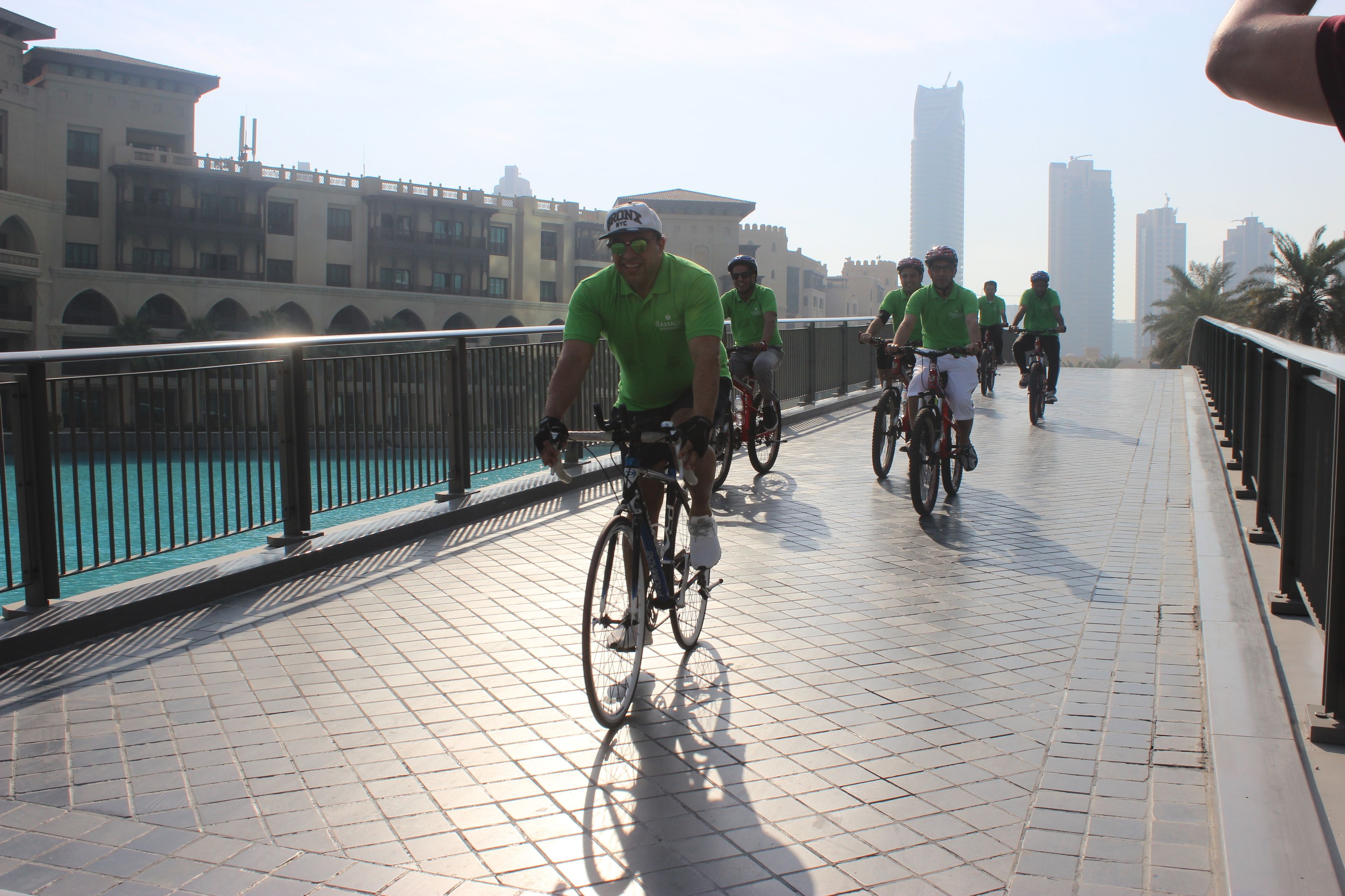 A group of cyclists on a bridge with a tiled walkway and metal railing.
