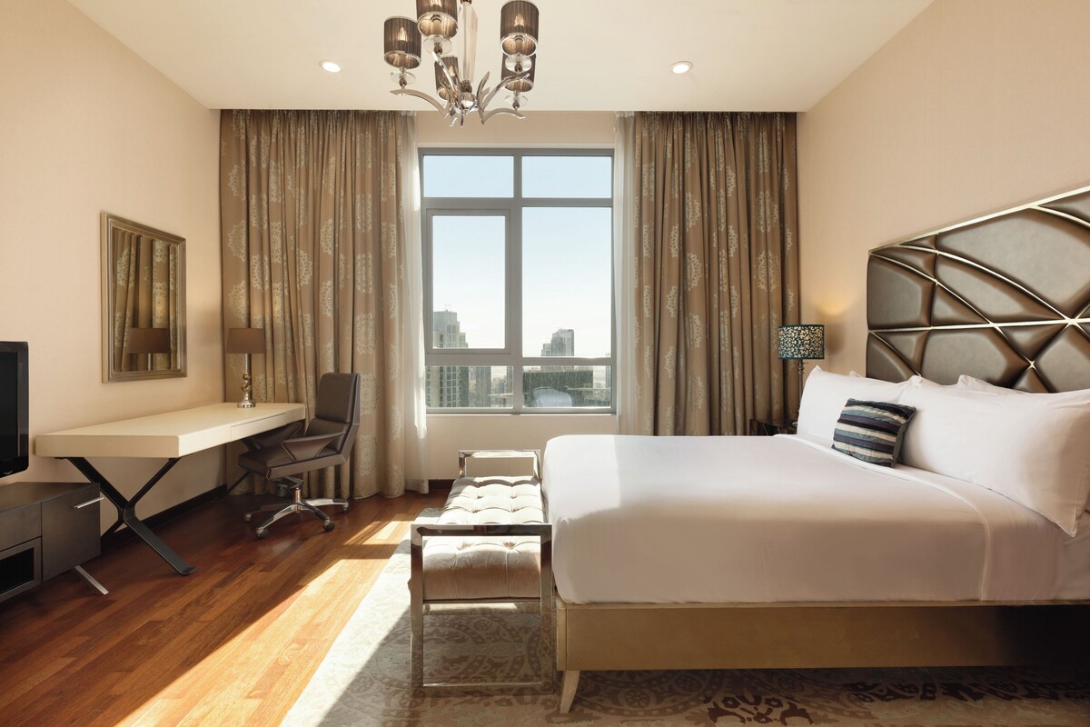 Een hotelkamer met een bed, bureau, stoel en uitzicht op de stad.