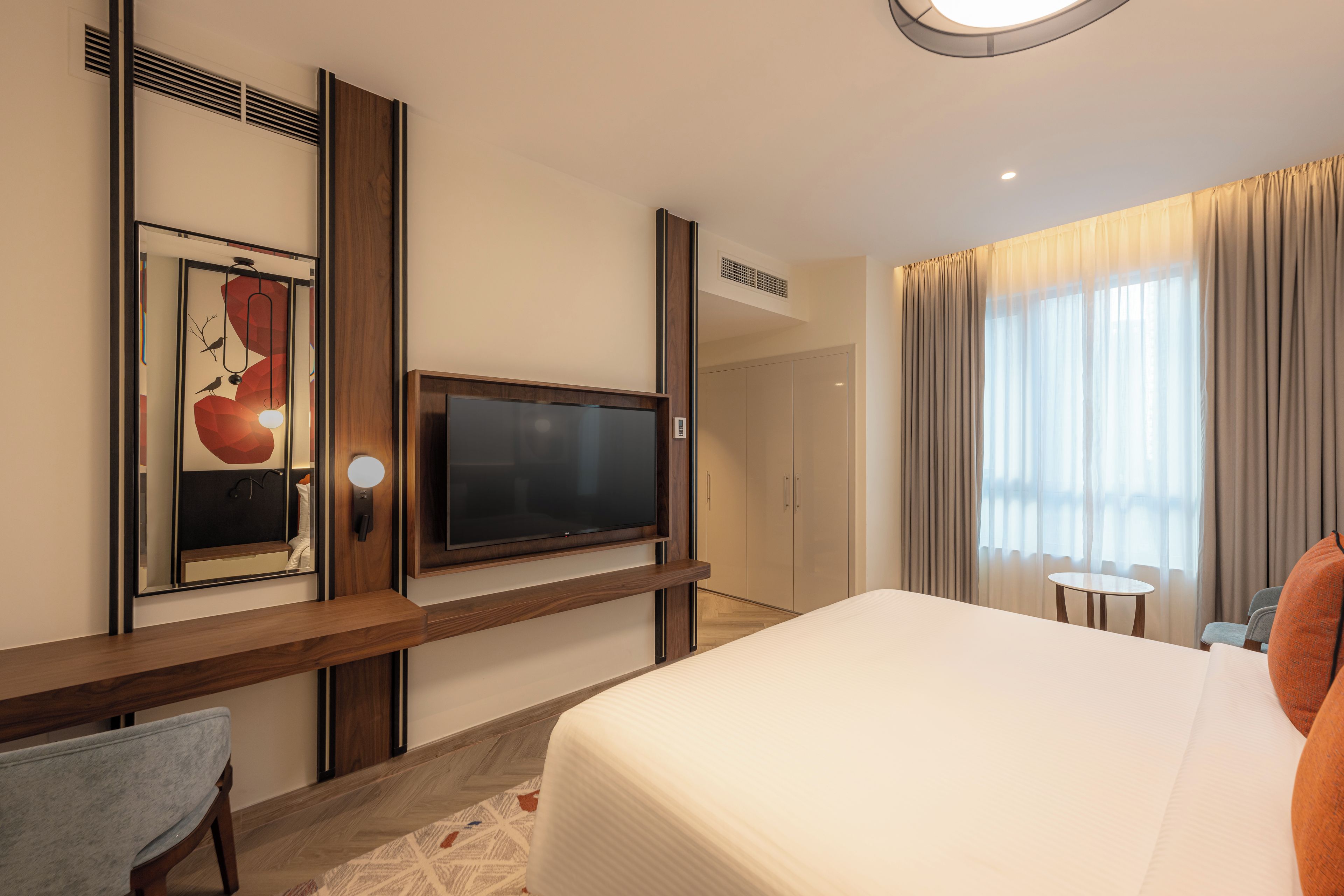 A hotel room with a large bed, a flat-screen TV mounted on a wooden panel, a small table, and a chair.