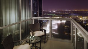 Een balkon met twee rieten stoelen, een glazen tafeltje en uitzicht op een stadsbeeld 's nachts.