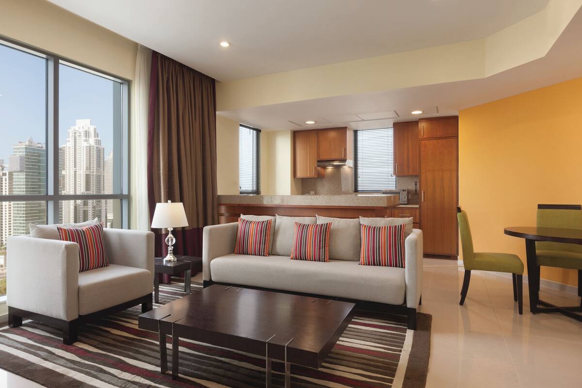 Een moderne hotelkamer met een bank, fauteuils, een eettafel en een keukenhoek.