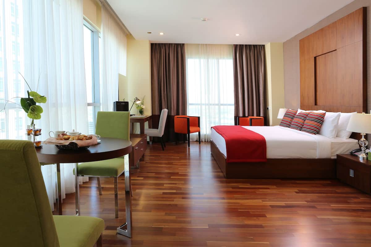 Een hotelkamer met een bed, een bureau met stoelen, een raam met gordijnen en een houten vloer.