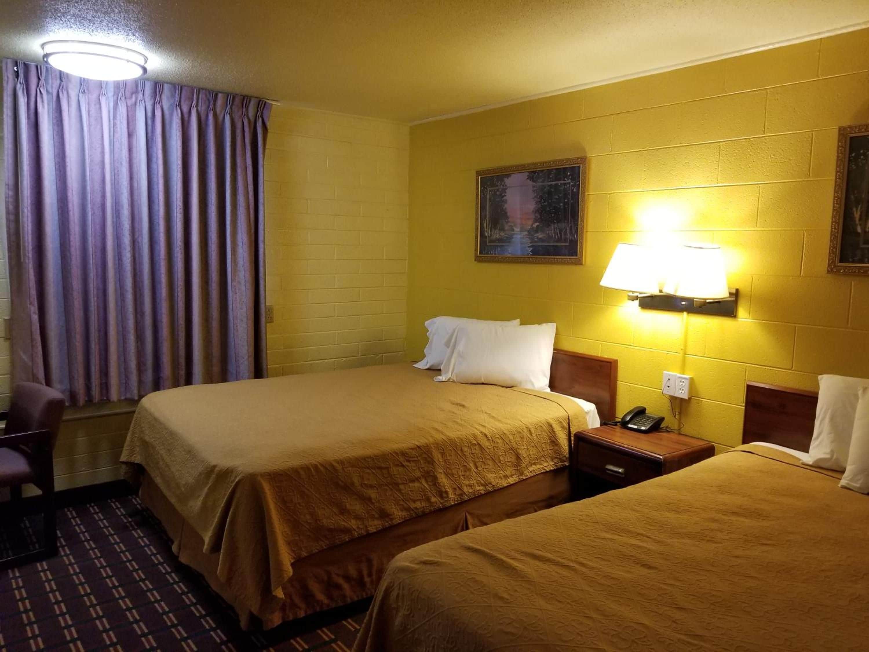 A hotel room with two beds, a chair, a nightstand with a phone, and a painting on the wall.