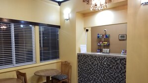 A hotel room with a dining area featuring a round table and chairs, a bar area with a patterned wall, and a window with blinds. - Motel 7 Rawlins (Rawlins)