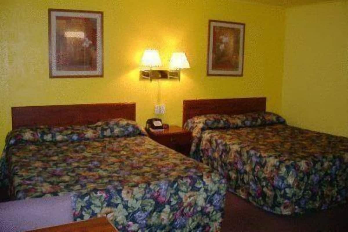 Habitación de hotel con dos camas, cada una con ropa de cama floral, una mesita de noche con lámpara y dos cuadros en la pared.