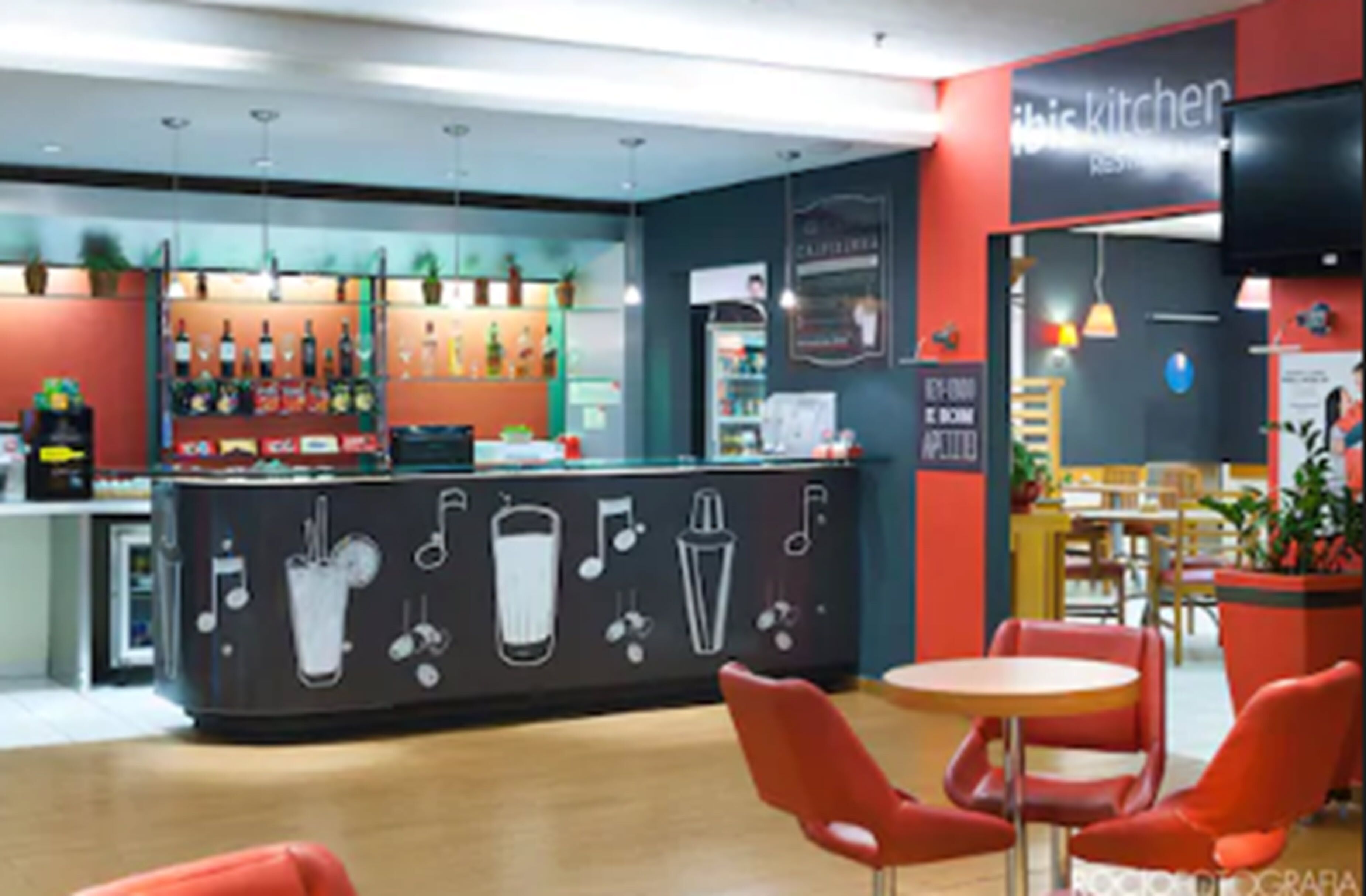 A modern bar area with a counter displaying various beverages and a menu. There are red chairs and tables in the seating area.
