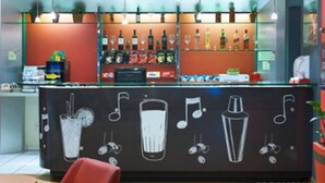 A bar area with a chalkboard displaying drink-related drawings, shelves with bottles, and a cash register. - ibis Uberlandia (Uberlandia)