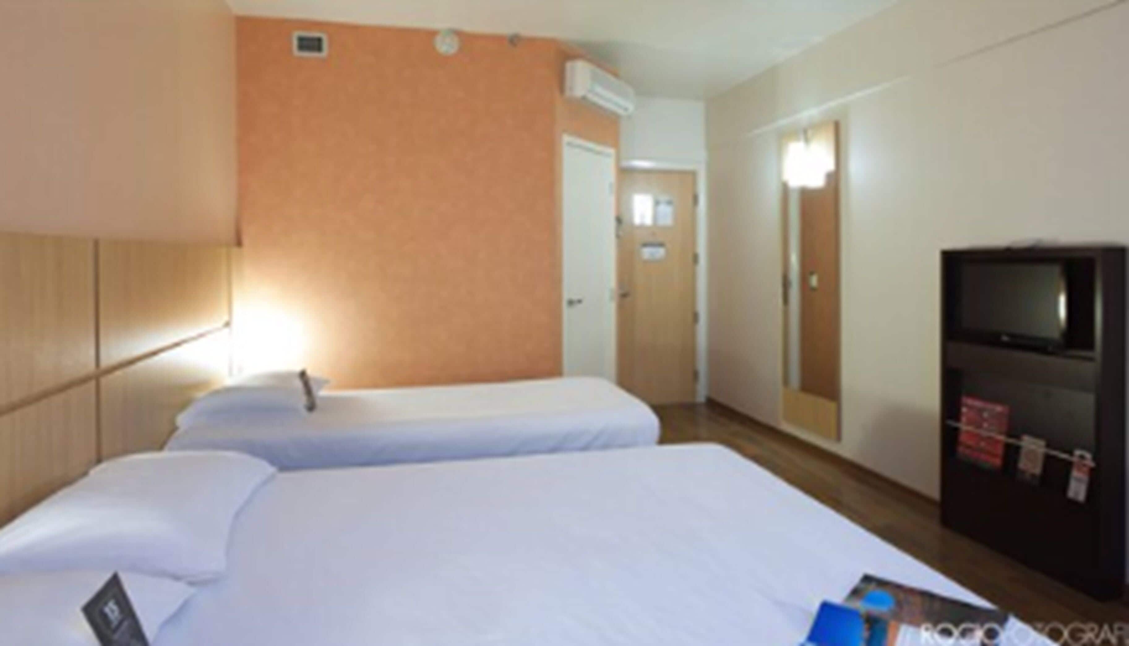Una habitación de hotel con dos camas individuales, un televisor y un espejo.
