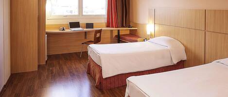 A hotel room with two beds, a desk with a laptop, a chair, and a window with curtains.