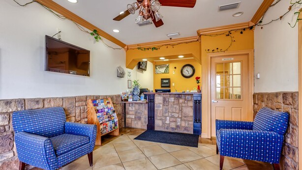 A lobby with two blue patterned chairs, a stone wall, a wooden ceiling fan, a reception desk, and a clock on the wall. - Quality Inn Brownsville (Brownsville)