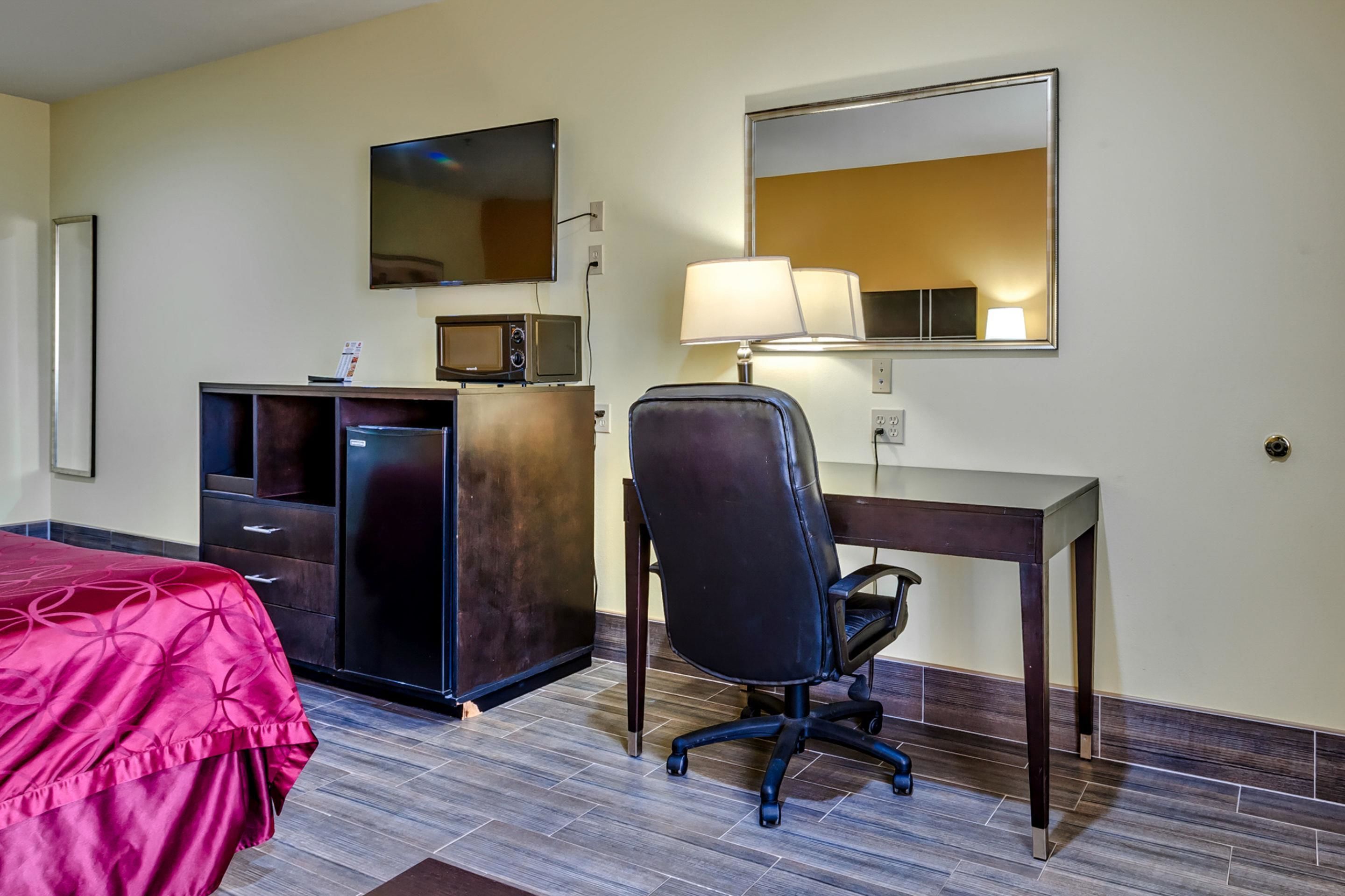 A hotel room with a bed, a desk, a chair, a TV, a microwave, and a lamp.