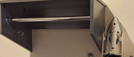 A corner of a room with a built-in ironing station, including an iron, a charging cable, and a storage compartment.