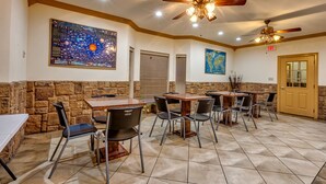 A dining area with stone walls, multiple tables and chairs, ceiling fans, and artwork on the walls. - Quality Inn Brownsville (Brownsville)