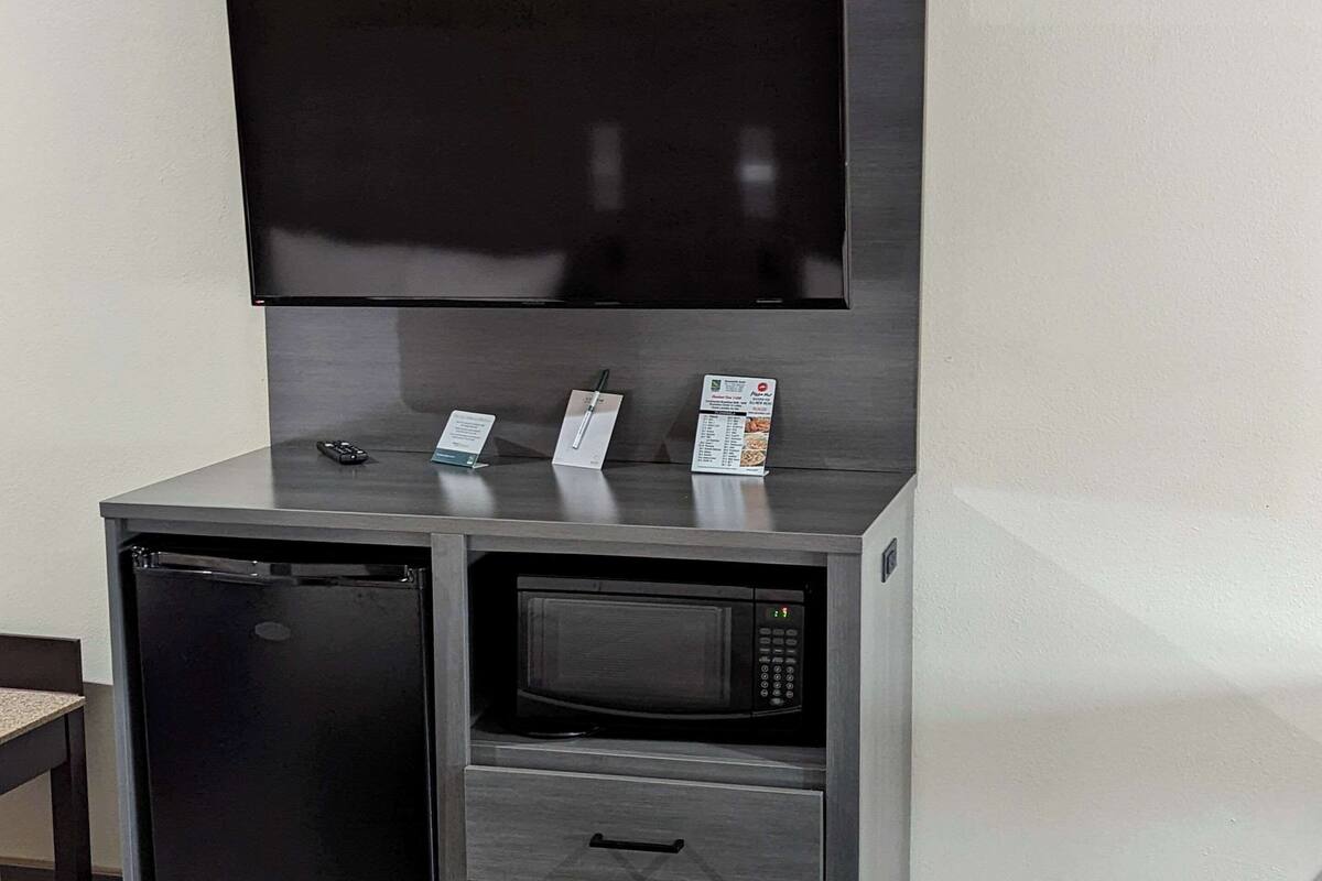 Une petite cuisine équipée d’un réfrigérateur, d’un four à micro-ondes et d’un téléviseur à écran plat fixé au mur.